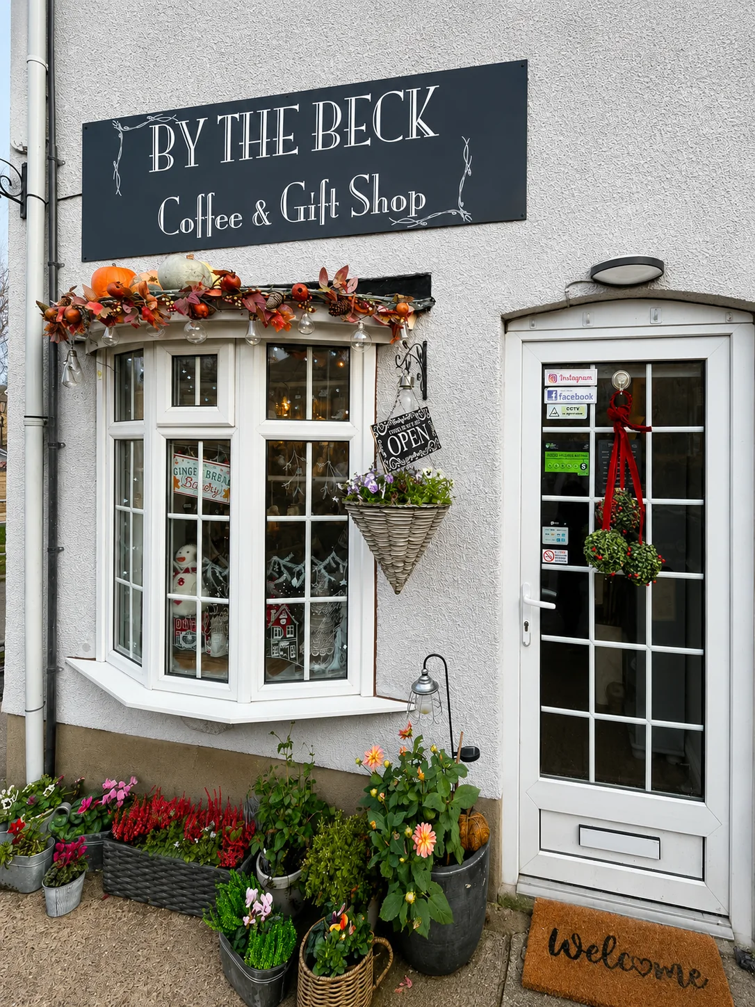 The By The Beck Coffee & Gift Shop sign, entrance and flower display
