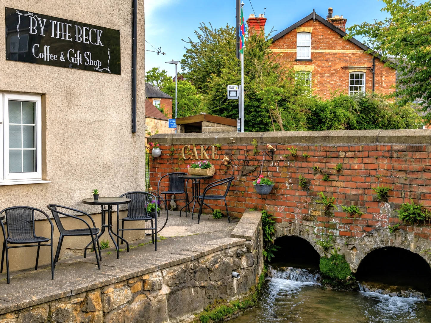 Outdoor tables beside the beck and the By The Beck shop sign
